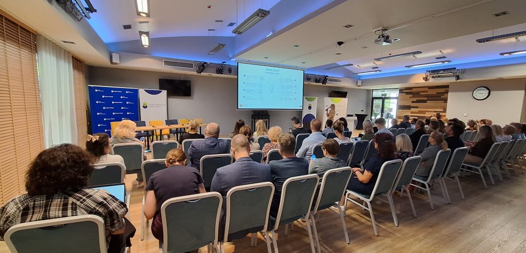 Sala konferencyjna z uczestnikami spotkania widziana od tyłu. Na środku ekran ze slajdem dot. śladów życia. Po prawej i lewej stronie ekranu rollup’y Urzędu Statystycznego.